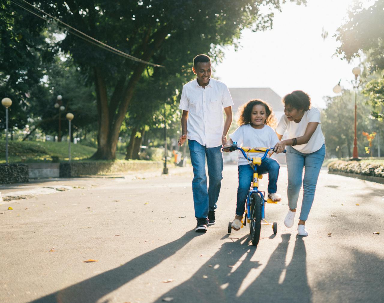 Services-03 Happy family teaching their child to cycle on a sunny day outdoors.