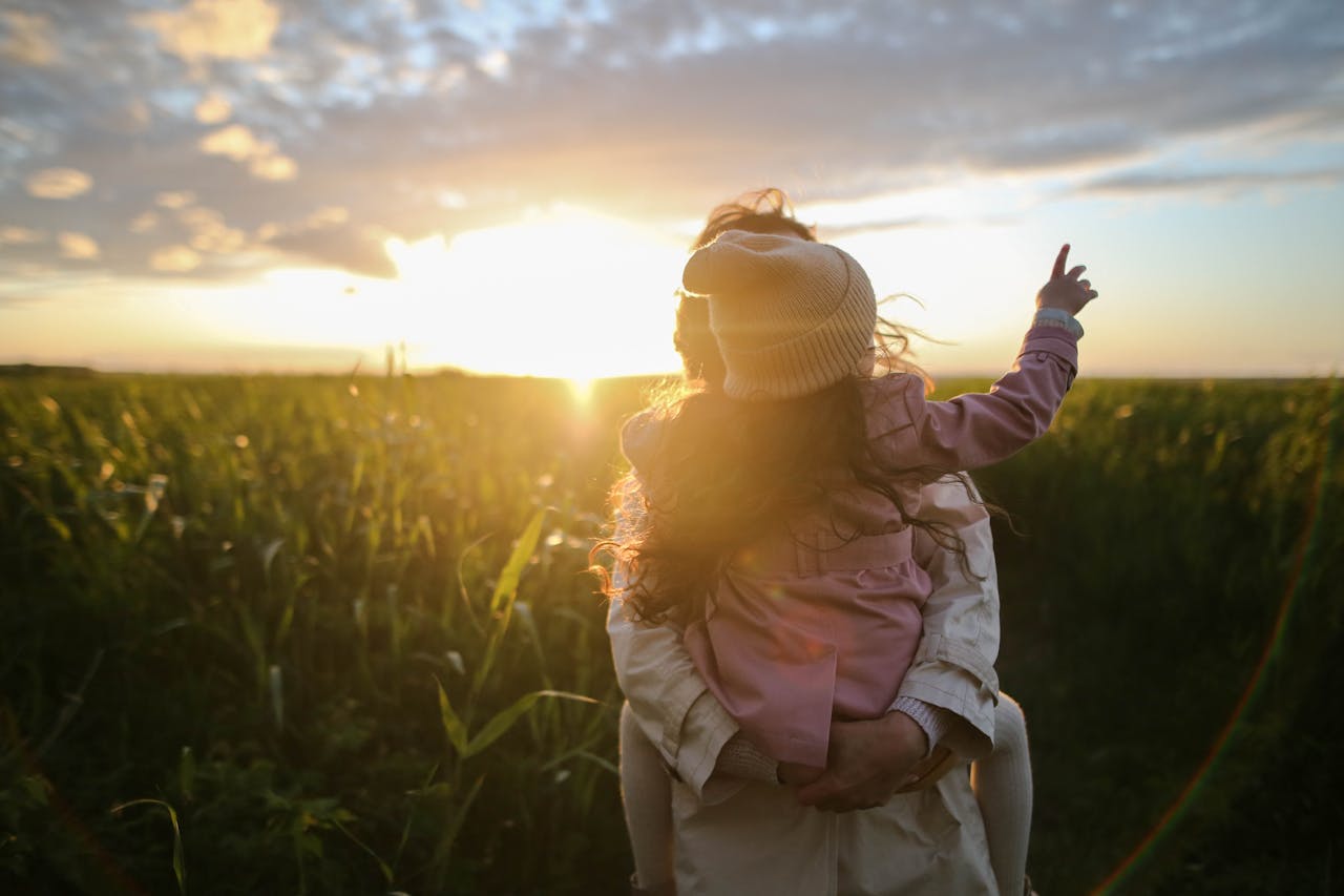 Services-01 A mother and daughter embrace and point at the sunset in a grassy field.